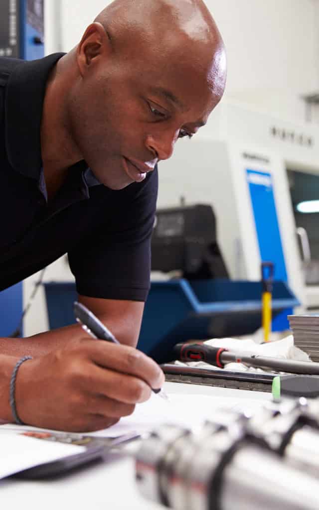 black male engineer working while taking notes with pen and paper
