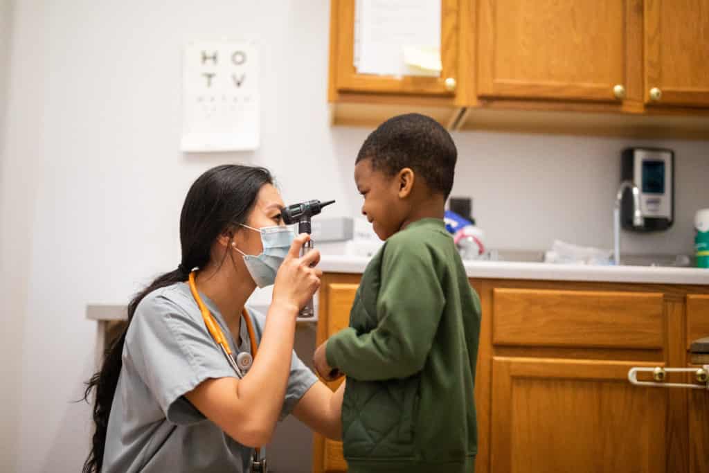 asian female nurse shows young black boy an otoscope during physical exam