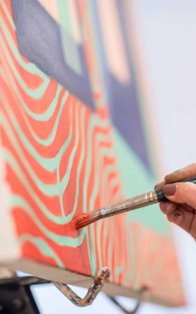 a hand holding a paint brush against a canvas with bright colors