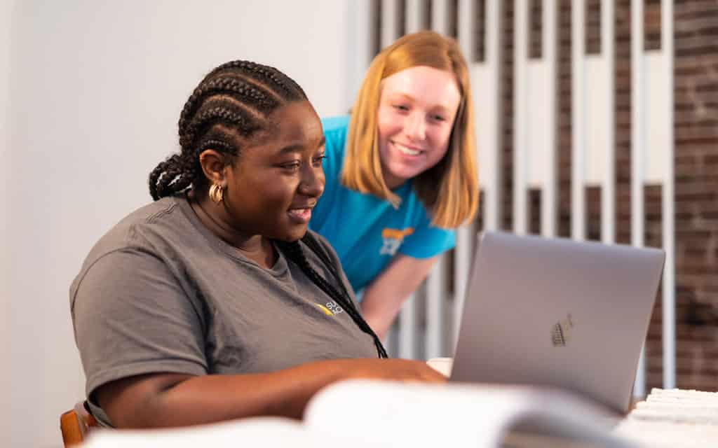 black female student and white red headed student smiling together at computer