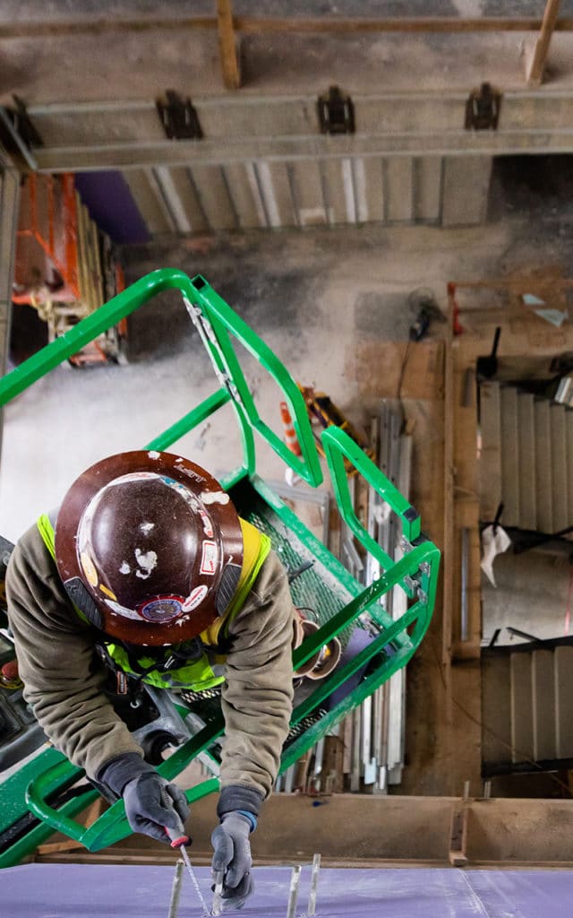 Birds Eye view of industrial worker wearing hardhat on lift working on building