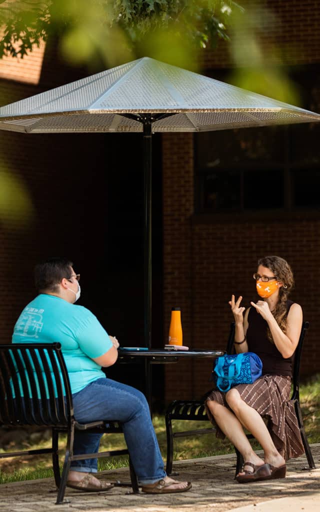 two people sitting outside at a table speaking with sign language