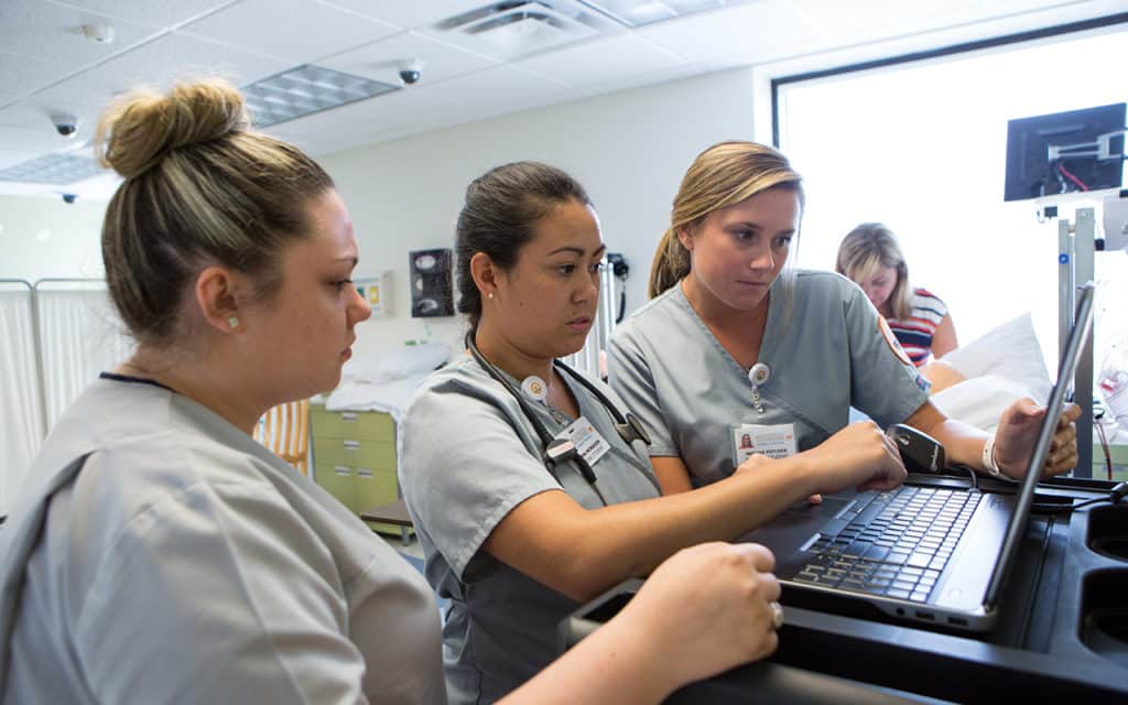 group of three female nurses reading patient information on hospital computer