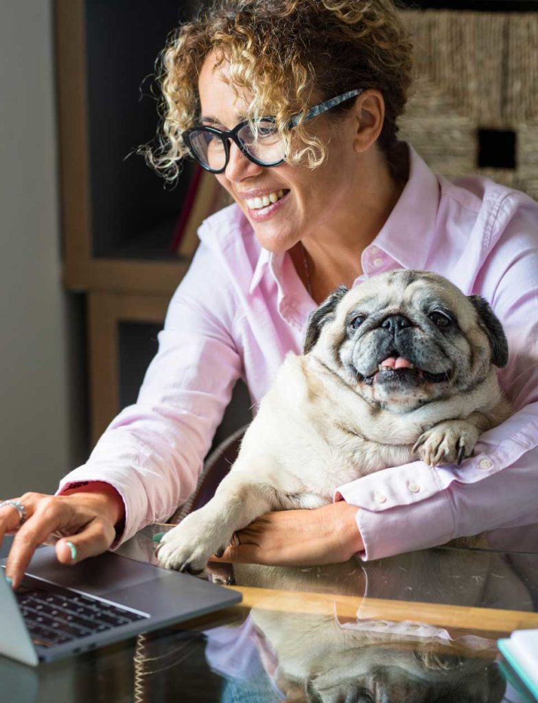 woman with glasses and curly hair holding a pug while studying on computer