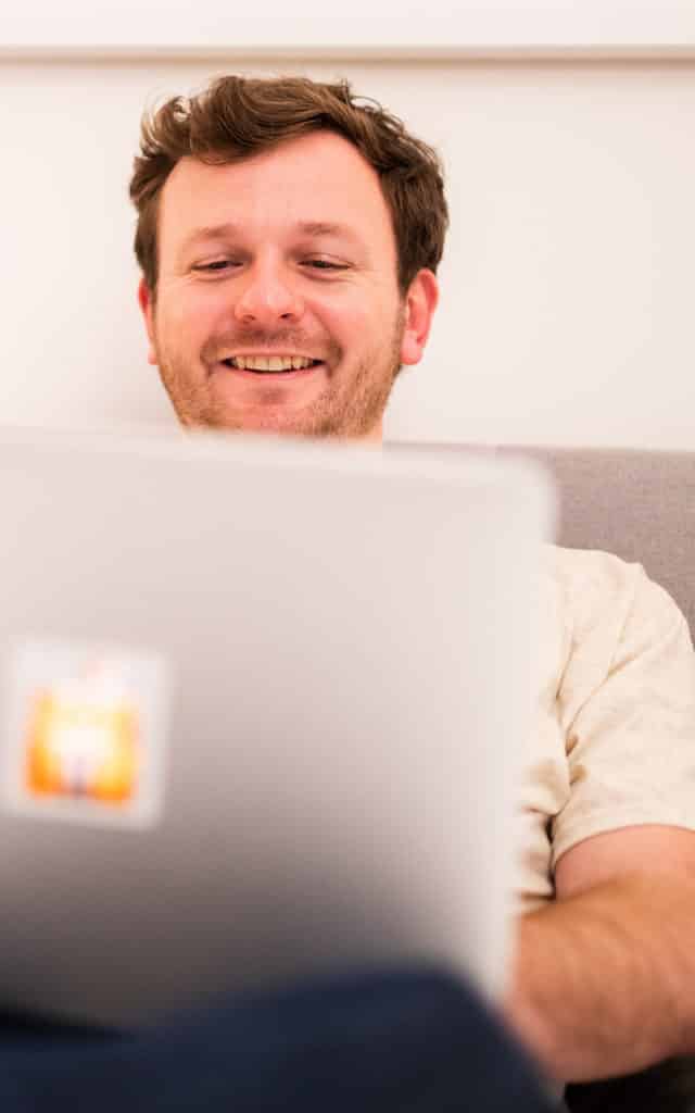 white male student sitting on couch working on laptop