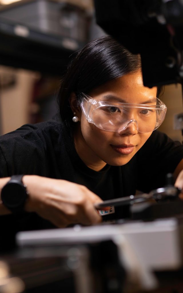asian female wearing safety goggles working on engineering equipment 
