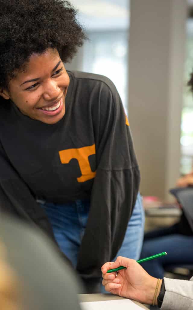 black female teacher smiling and wearing grey sweater with orange t