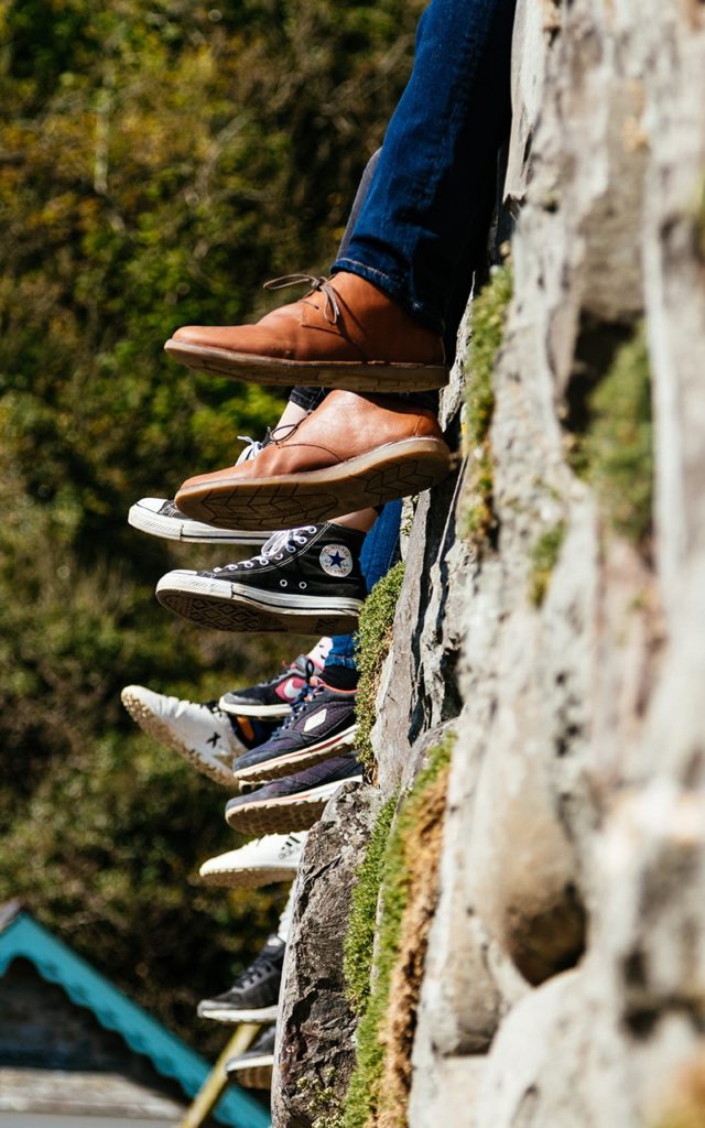 six pairs of feet hanging off a stonewall 