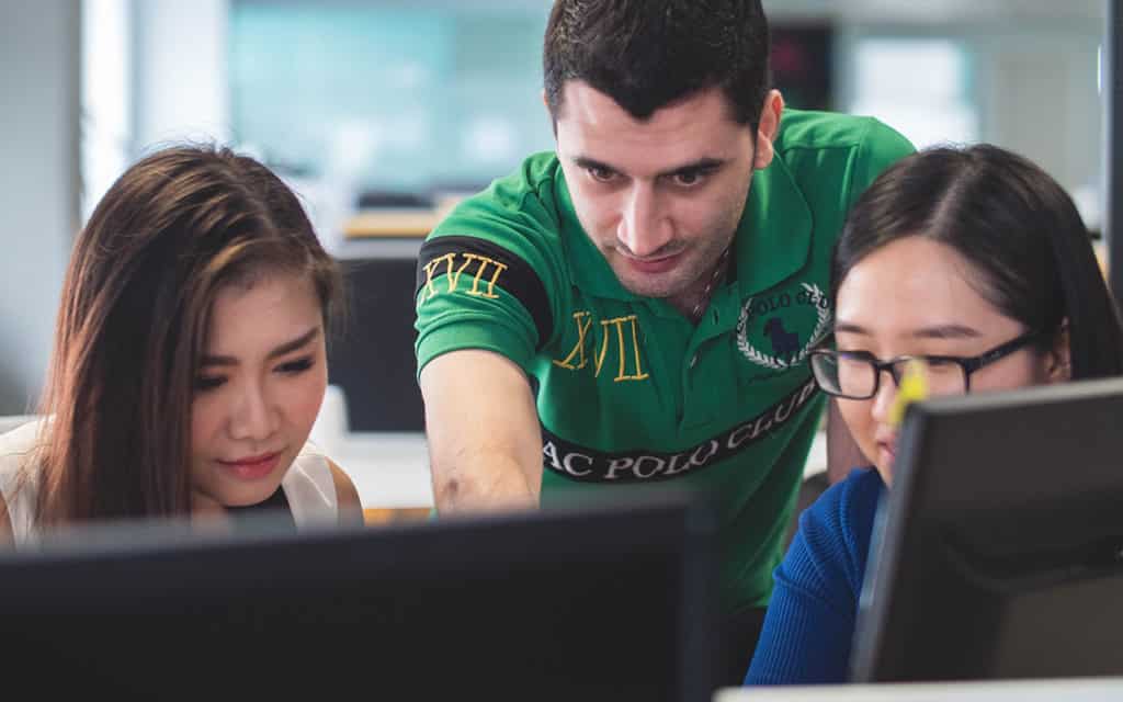 two female asian students with white male student working on computer