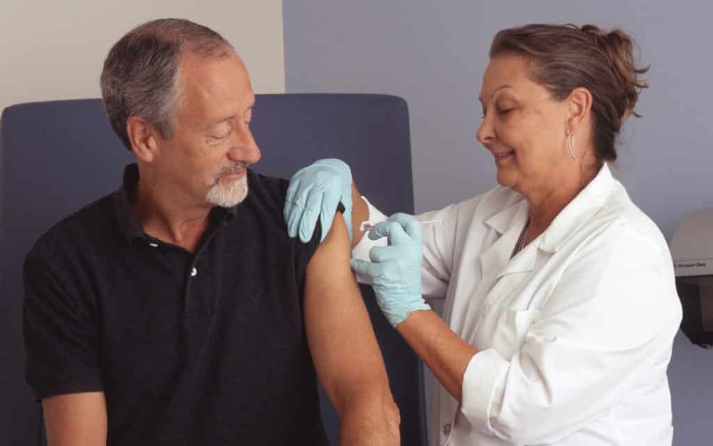 white female nurse practitioner gives vaccine to older white male
