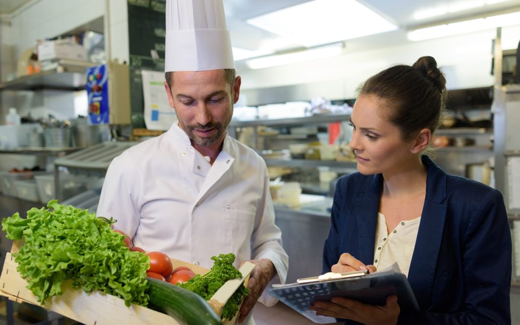 white male chef speaking with white woman holding a clipboard  