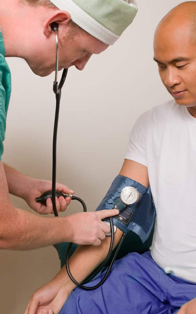 white male doctor using blood pressure cuff on asian male patient 