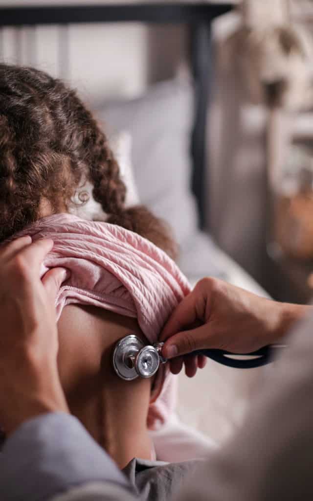 hands holding stethoscope against young patient's back