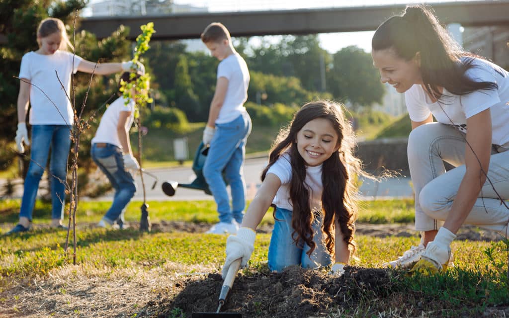 woman and school aged children plant trees in community garden