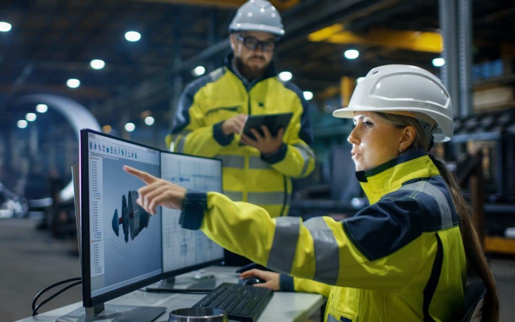 white women and man wearing hardhats on job site looking at computer screen