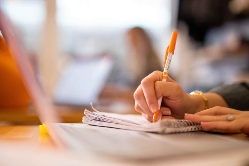 close up of student using orange pen to write in notepad