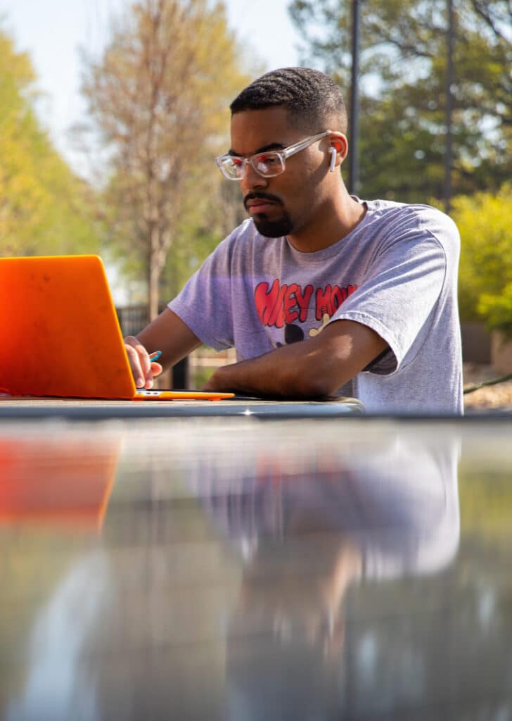black male student studying outside on laptop