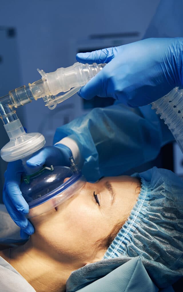 gloved hands holding mask around white females mouth during surgery